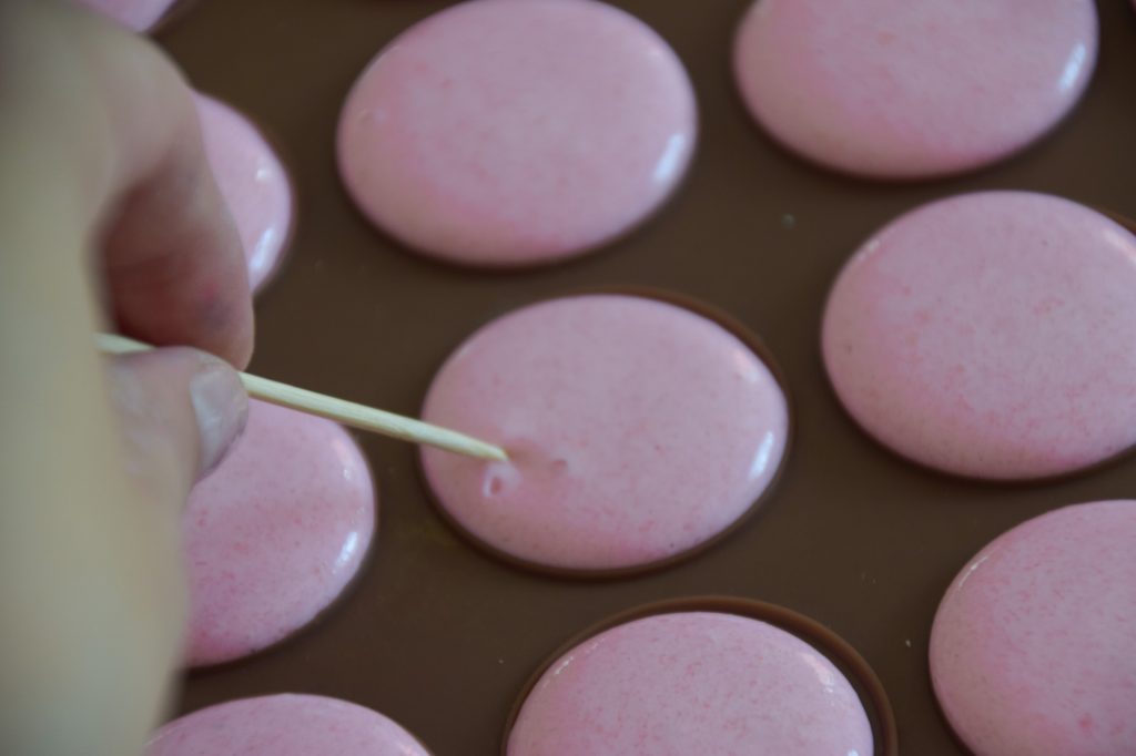 Fixing the piped macaron batter with a toothpick and breaking the air bubbles