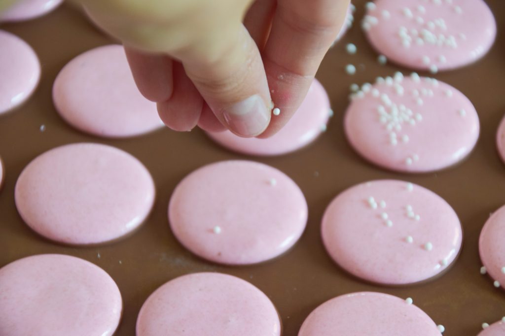 Putting sprinkles over the light pink macaron shells