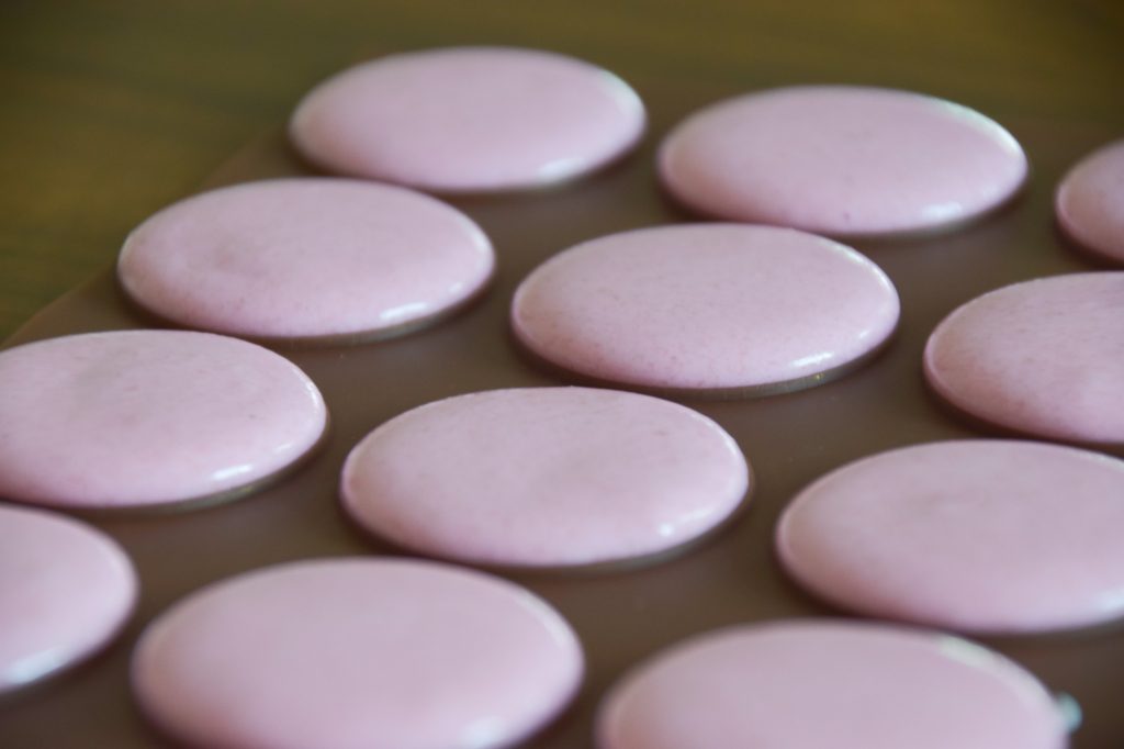 Pink macarons piped to the silicone mat