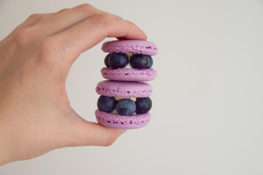 Purple blueberry macarons with fresh blueberries between fingers
