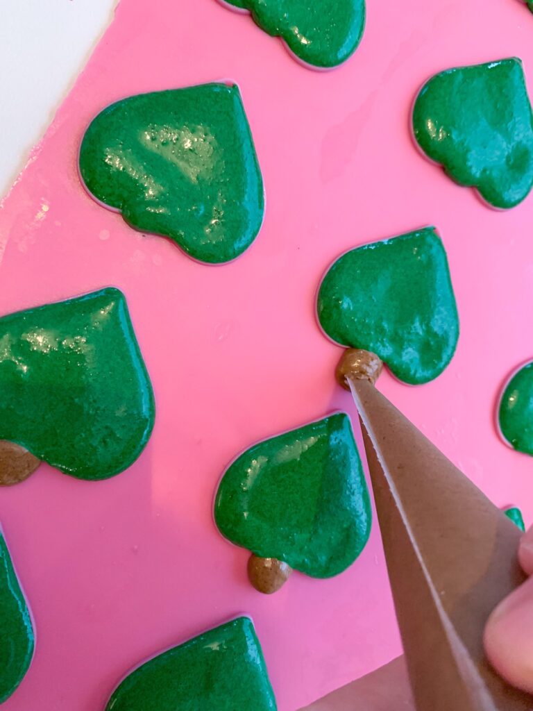 Green Christmas tree macarons on a silicone mat piping tree trunks