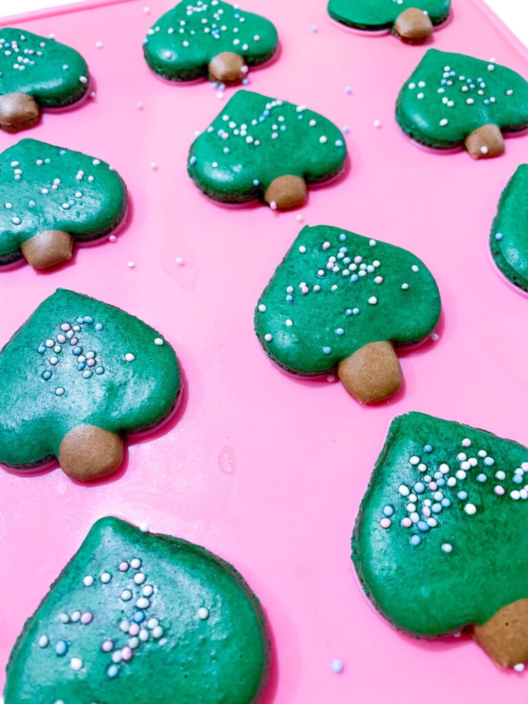 Green Christmas tree macarons on a silicone mat with sprinkles